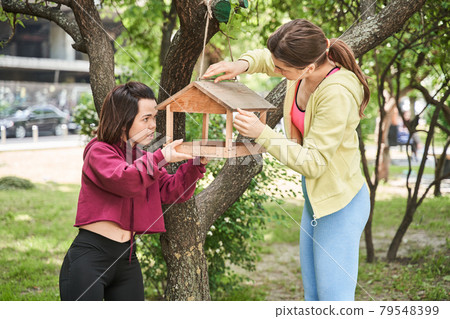 Midget woman adjusting birds feeder at the tree with her best friend 79548399
