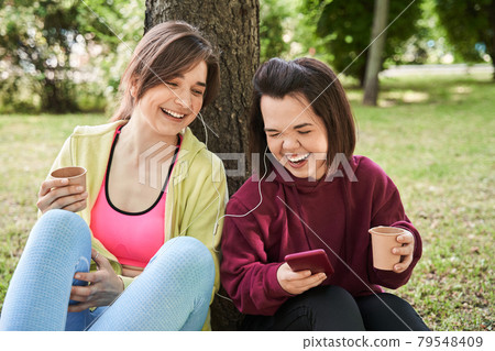 Girls laughing out loud and turning on songs at her smartphone Girls laughing out loud and turning on songs at her smartphone 79548409