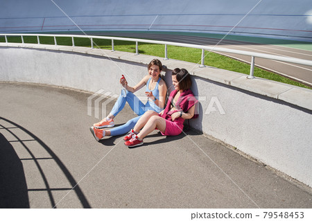 Girls in sportswear relaxing after a workout or run and having conversation Girls in sportswear relaxing after a workout or run and having conversation 79548453