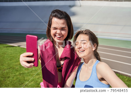 Girls looking at the smartphone camera and squinting of the sun Girls looking at the smartphone camera and squinting of the sun 79548455