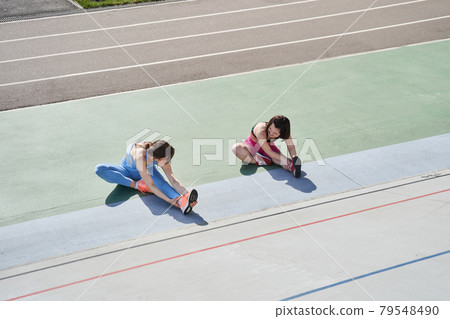 Girls doing stretching on the stadium while looking at the each other Girls doing stretching on the stadium while looking at the each other 79548490