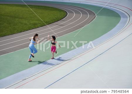 Woman running to meet to her best friend running on a treadmill at the stadium Woman running to meet to her best friend running on a treadmill at the stadium 79548564