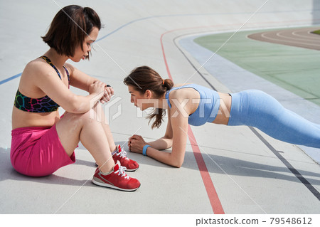 Woman standing at the plank while her midget best friend looking at the fitness tracker 79548612