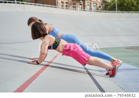 Woman doing planking exercise at the stadium at the company of her midget best friend Woman doing planking exercise at the stadium at the company of her midget best friend 79548632
