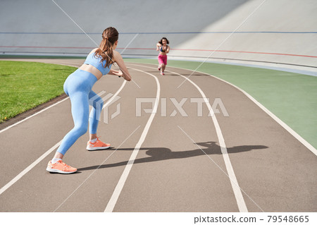 Girl waiting at the finish to her midget friend while she running at the stadium Girl waiting at the finish to her midget friend while she running at the stadium 79548665