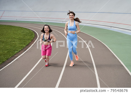 Women in sports outfits jog on running track in city stadium in sunny morning Women in sports outfits jog on running track in city stadium in sunny morning 79548676