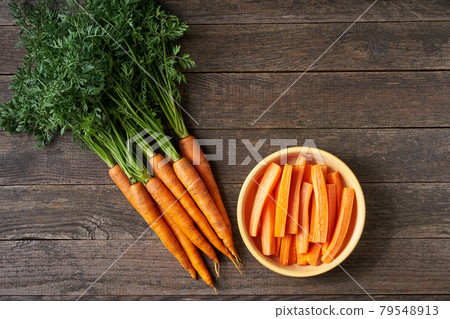 Carrot sticks in a wooden bowl on a table, top view, rustic style. Carrot sticks in a wooden bowl on a table, top view, rustic style. 79548913