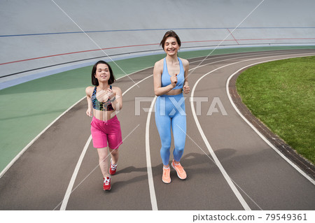 Women in sports outfits jog on running track in city stadium in sunny morning Women in sports outfits jog on running track in city stadium in sunny morning 79549361