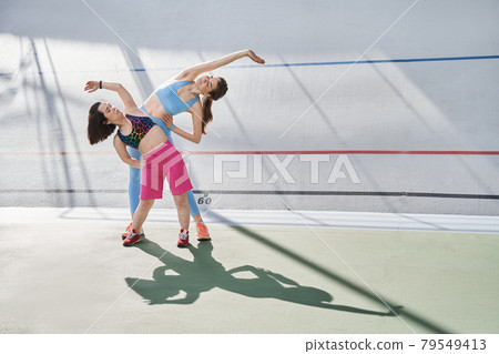 Diverse girls are doing exercises on a sunny summer morning on grass sports stadium 79549413