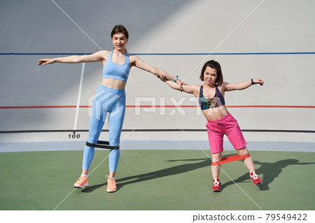 Best friends holding at the hands and training at the stadium with elastic bands Best friends holding at the hands and training at the stadium with elastic bands 79549422