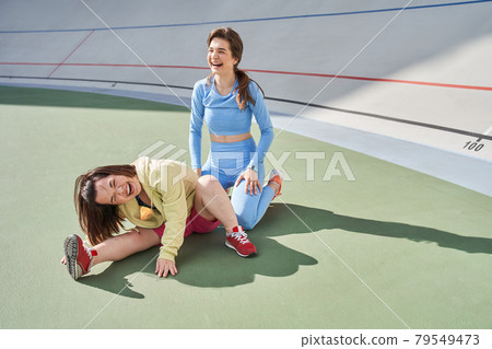 Midget woman stretching at the stadium while her best friend or trainer laughing out loud Midget woman stretching at the stadium while her best friend or trainer laughing out loud 79549473