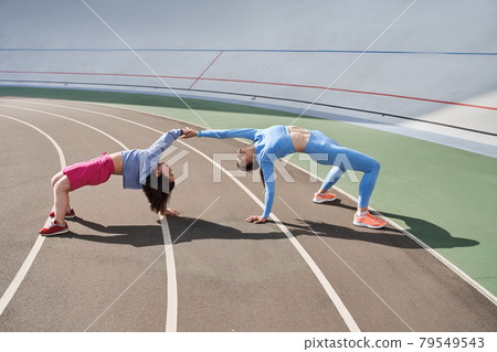 Friends standing in the bridge position and having fun while training at the stadium 79549543