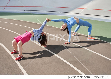 Friends standing in the bridge position and having fun while training at the stadium Friends standing in the bridge position and having fun while training at the stadium 79549553