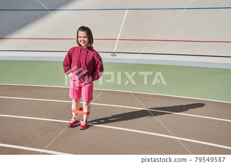Woman standing at the stadium and training her legs with elastic bands Woman standing at the stadium and training her legs with elastic bands 79549587
