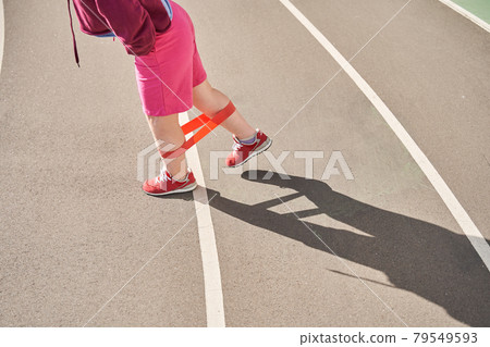 Woman with genetical disorder stretching her legs while exercising at the stadium Woman with genetical disorder stretching her legs while exercising at the stadium 79549593