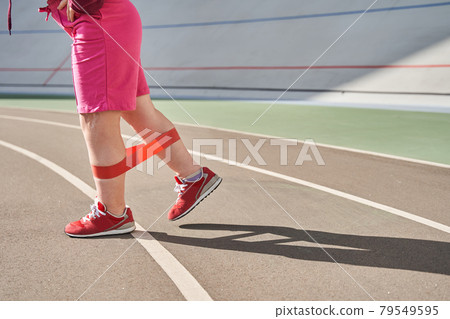 Woman with genetical disorder stretching her legs while exercising at the stadium Woman with genetical disorder stretching her legs while exercising at the stadium 79549595