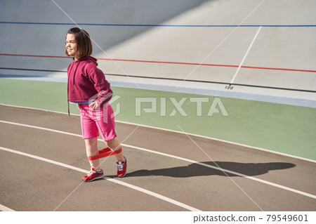 Woman squints of the sun while standing at the stadium and training her legs Woman squints of the sun while standing at the stadium and training her legs 79549601