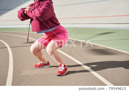 Woman wearing sports wear exercising in outdoor arena while doing squats 79549623