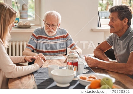 Two senior man sitting at the table with their caregiver and chatting 79550891