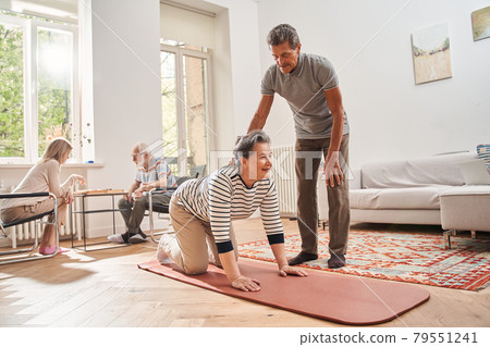 Senior man helping doing morning exercises to his female friend Senior man helping doing morning exercises to his female friend 79551241