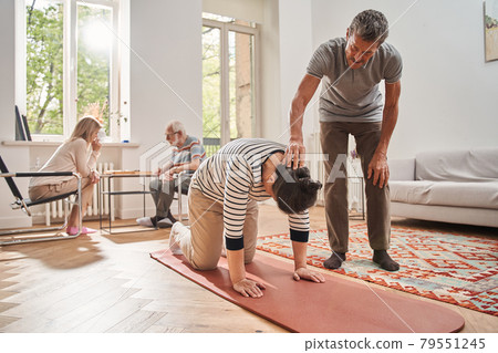 Senior man helping doing morning exercises to his female friend Senior man helping doing morning exercises to his female friend 79551245