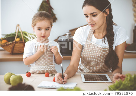 Happy woman and her daughter are searching for new recipes for a delicious family feasting. Christmas, New year, Thanksgiving, Anniversary, Mothers Day. Healthy meal cooking concept 79551870