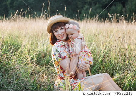 young beautiful woman sitting on the grass with her little cute daughter in the field on summer day young beautiful woman sitting on the grass with her little cute daughter in the field on summer day 79552215