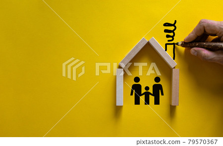 Conceptual image of family values and adoption. House from wooden blocks on beautiful yellow background. Male hand draws with black pencil chimney and smoke. 79570367