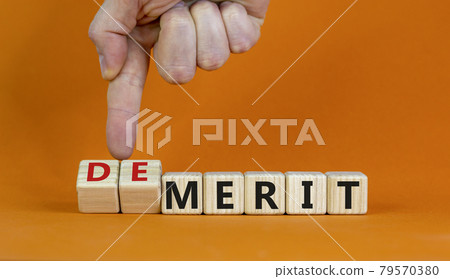 Demerit or merit symbol. Businessman turns wooden cubes and changes words 'demerit' to 'merit'. Beautiful orange background, copy space. Business and demerit or merit concept. 79570380