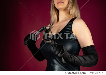 Beautiful young woman in a latex dress posing with a whip in her hands 79570714