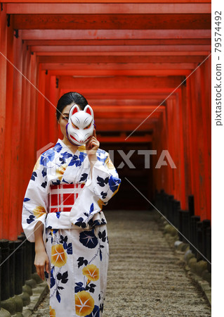 A young woman in a yukata under the red torii gate of Fushimi Inari Shrine A young woman in a yukata under the red torii gate of Fushimi Inari Shrine 79574492