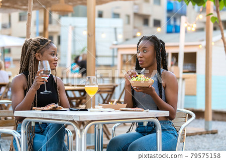 Latina women enjoying tasty takeaway food at an outdoors terrace Latina women enjoying tasty takeaway food at an outdoors terrace 79575158