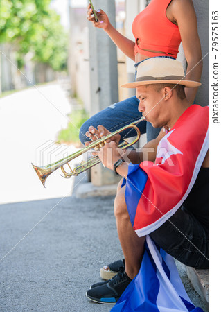 Latino man playing the trumpet next to latina woman checking her phone Latino man playing the trumpet next to latina woman checking her phone 79575163