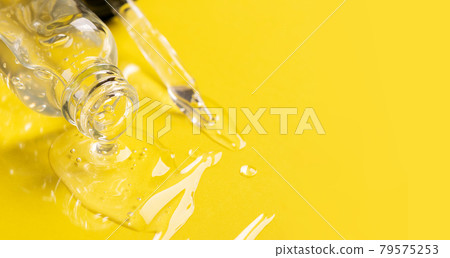 Cosmetic liquid gel serum lubricant flows out of glass bottle dropper dropper yellow background. Face and body care 79575253