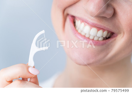 Close-up portrait of a beautiful caucasian woman with a flawless smile holding a toothpick with dental floss on a white background Close-up portrait of a beautiful caucasian woman with a flawless smile holding a toothpick with dental floss on a white background 79575499