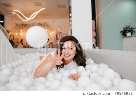an attractive woman in white clothes lies in a dry pool with white balls. an attractive woman in white clothes lies in a dry pool with white balls. 79576958