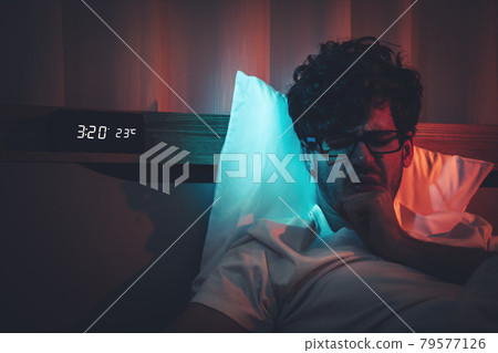 Insomnia sleepless man having a problem sleeping in late night with alarm clock telling late night time on his bed. Insomnia sleepless man having a problem sleeping in late night with alarm clock telling late night time on his bed. 79577126