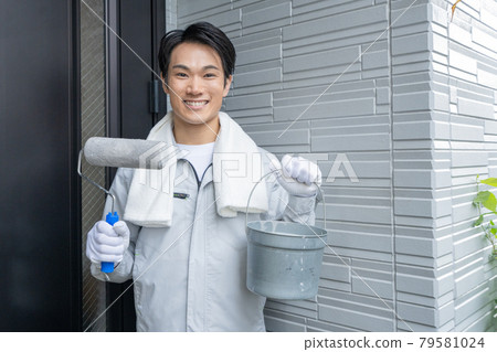 A young male painter who finishes painting the exterior walls and smiles in front of the entrance 79581024