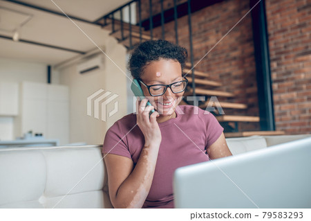 A woman in eyeglasses working on a laptop and talking on the phone 79583293