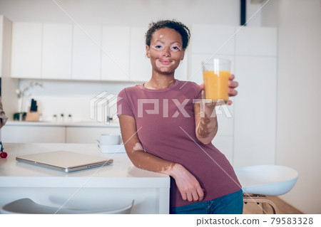 A dark-skinned woman holding a glass of orange juice A dark-skinned woman holding a glass of orange juice 79583328