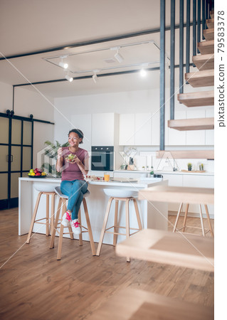 A dark-skinned woman sitting in the kitchen and eating salad 79583378