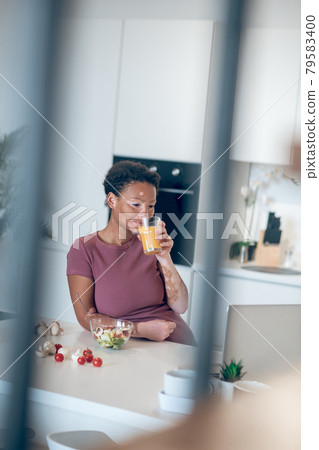 A dark-skinned woman drinking an orange juice 79583400