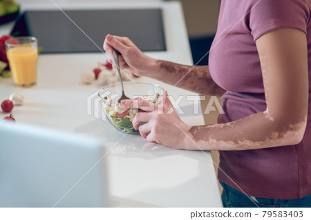 A dark-skinned woman eating salad and watching something on laptop 79583403
