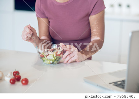 A dark-skinned woman eating salad and watching something on laptop 79583405