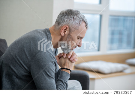 A gray-haired man sitting with eyes closed and saying the payers 79583597