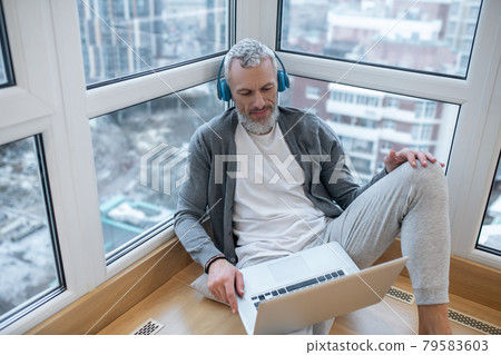 A mature man with a laptop and in headphones listening to something on internet A mature man with a laptop and in headphones listening to something on internet 79583603