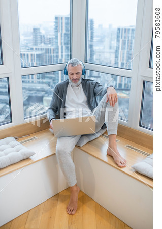 A mature man with a laptop and in headphones listening to something on internet 79583608