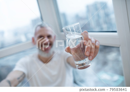 A bearded mature man holding a glass with water A bearded mature man holding a glass with water 79583641