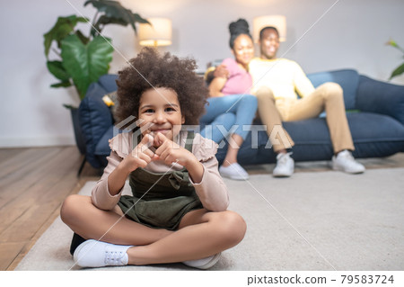 Girl showing heart with fingers and parents behind Girl showing heart with fingers and parents behind 79583724