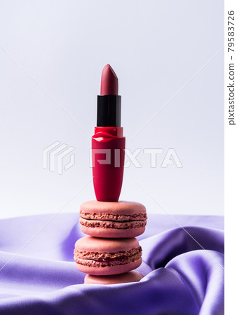 Red fashion lipstick and pink macaroons on purple silk fabric and gray background Red fashion lipstick and pink macaroons on purple silk fabric and gray background 79583726